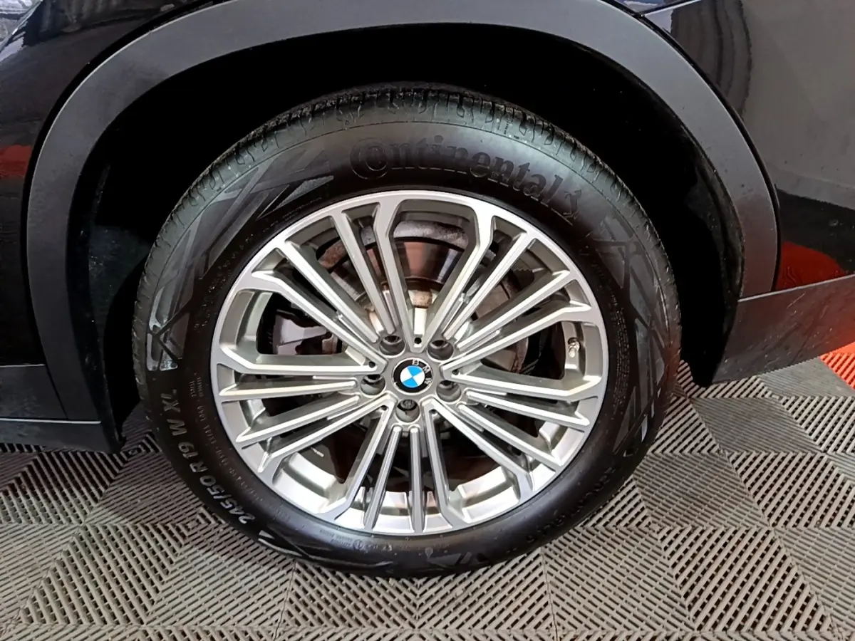 Gros plan sur la roue avant droite d’un BMW X3 noir, mettant en valeur la jante alliage multi-branches argentée.