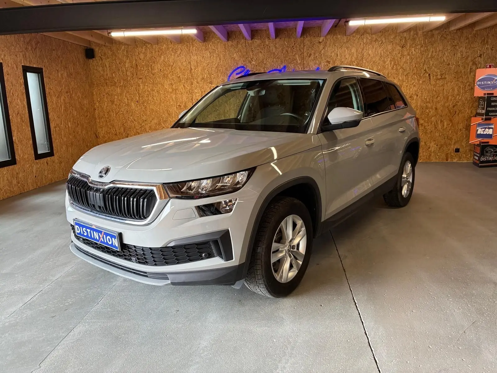 Vue 3/4 avant droite d'un Skoda Kodiaq gris clair 2023 en intérieur avec calandre noire et jantes argentées.