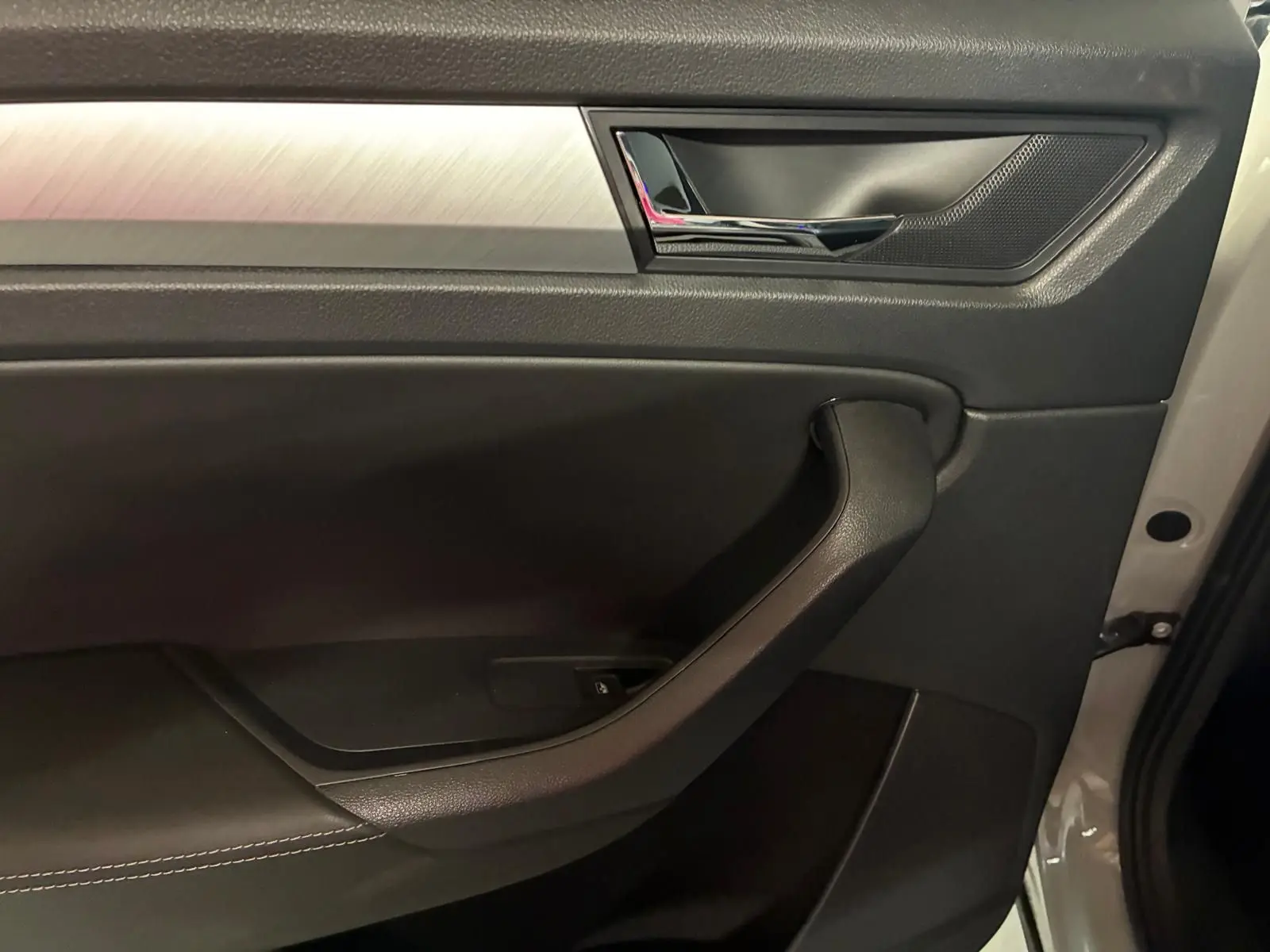 Vue rapprochée de la porte intérieure côté droit d’un Skoda Kodiaq gris clair 2023, avec poignée noire et insert métal brossé.