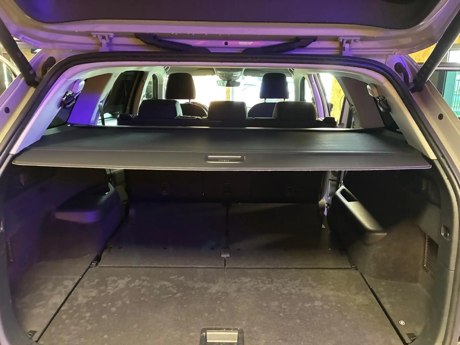 Vue arrière du coffre ouvert d'un Skoda Kodiaq gris clair 2023, avec cache-bagages déployé et sièges arrière visibles.