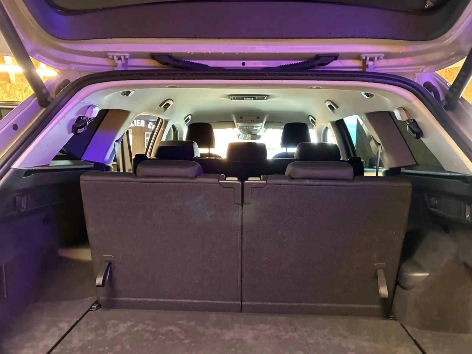 Vue arrière intérieure du coffre ouvert d’un Skoda Kodiaq gris clair 2023, montrant la troisième rangée de sièges en tissu noir relevée.