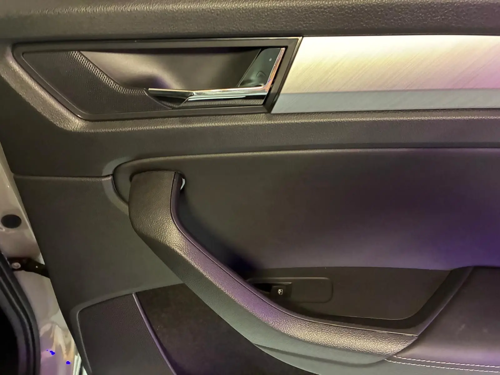 Détail de la porte intérieure côté gauche du Skoda Kodiaq gris clair, avec poignée noire et insert aluminium brossé.