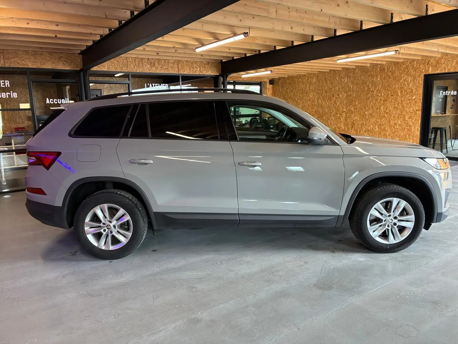 Vue latérale droite d'un Skoda Kodiaq gris clair 2023, SUV 7 places avec jantes alliage et vitres teintées, en intérieur.