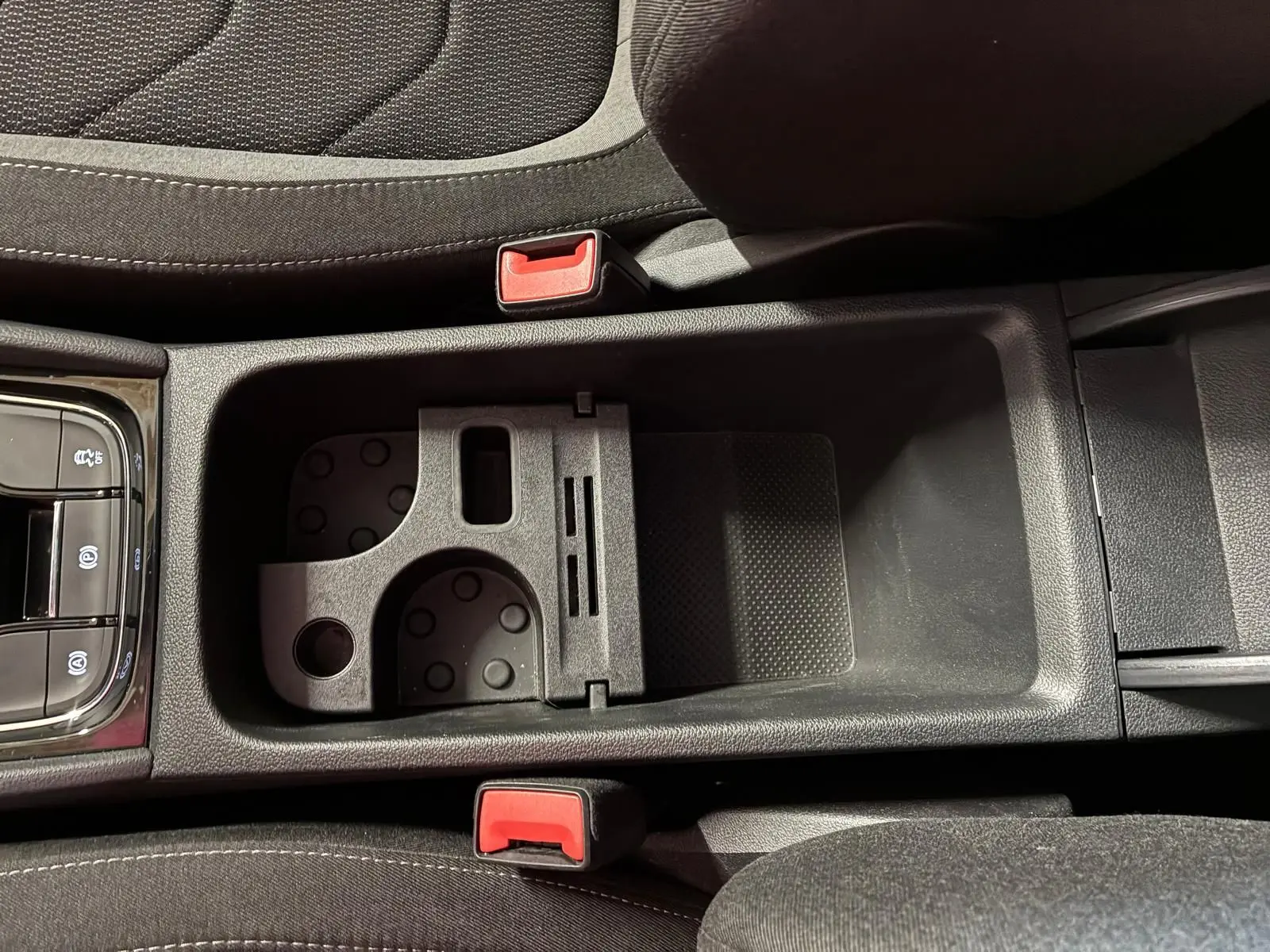 Vue rapprochée de la console centrale noire du Skoda Kodiaq 2023, montrant porte-gobelets et accoudoir entre sièges tissu.