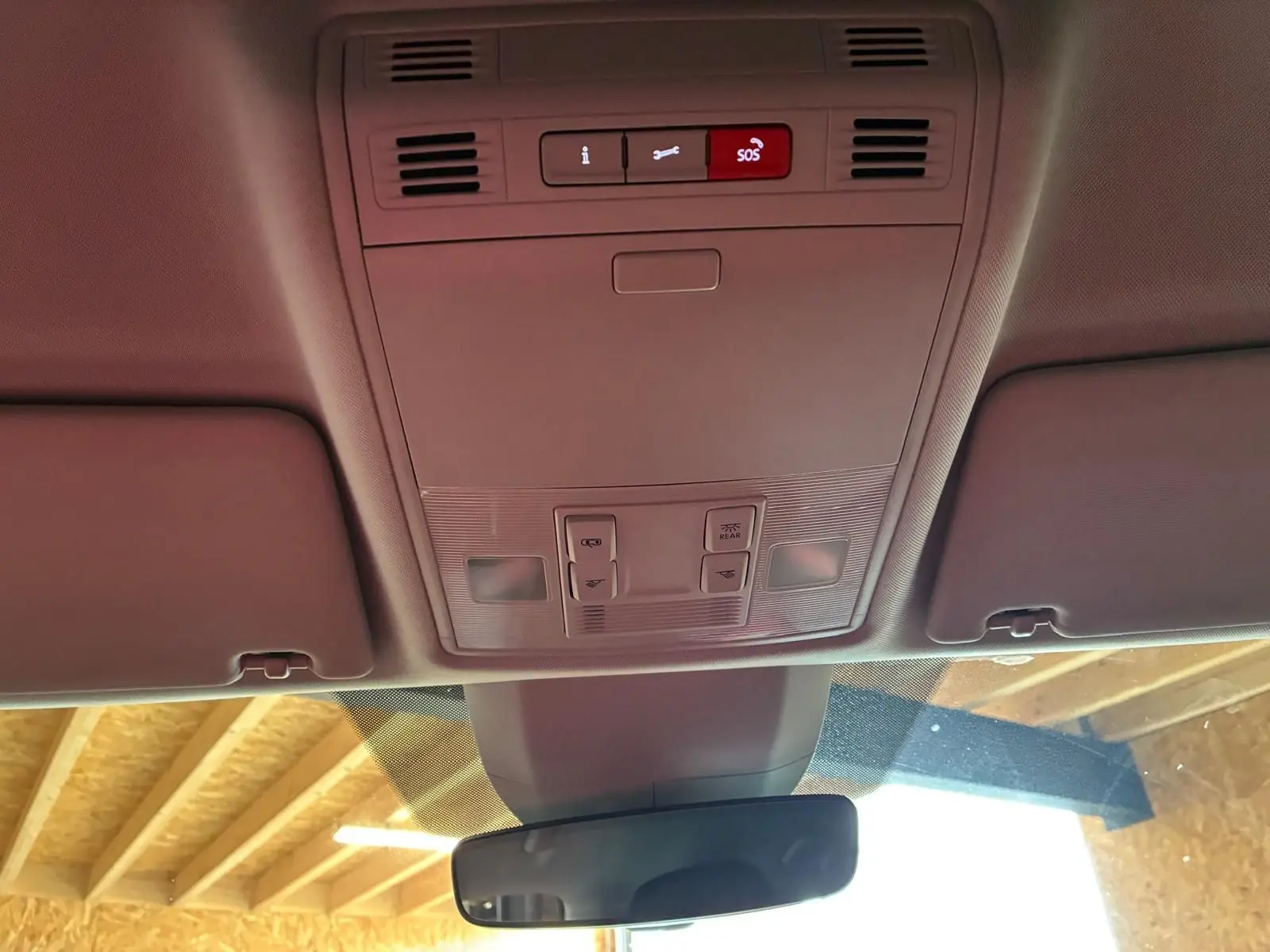 Vue intérieure du plafond avant d'un Skoda Kodiaq gris clair 2023, montrant les commandes d'éclairage et le bouton SOS.