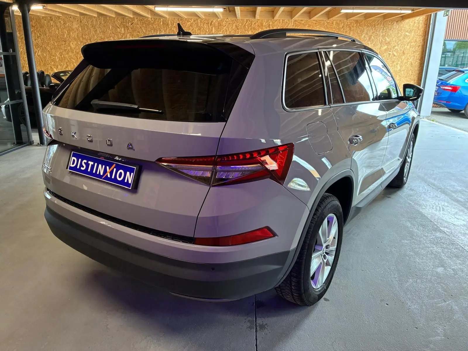 Vue 3/4 arrière droite d'un Skoda Kodiaq gris clair 2023 stationné en intérieur, avec vitres teintées et jantes alliage.