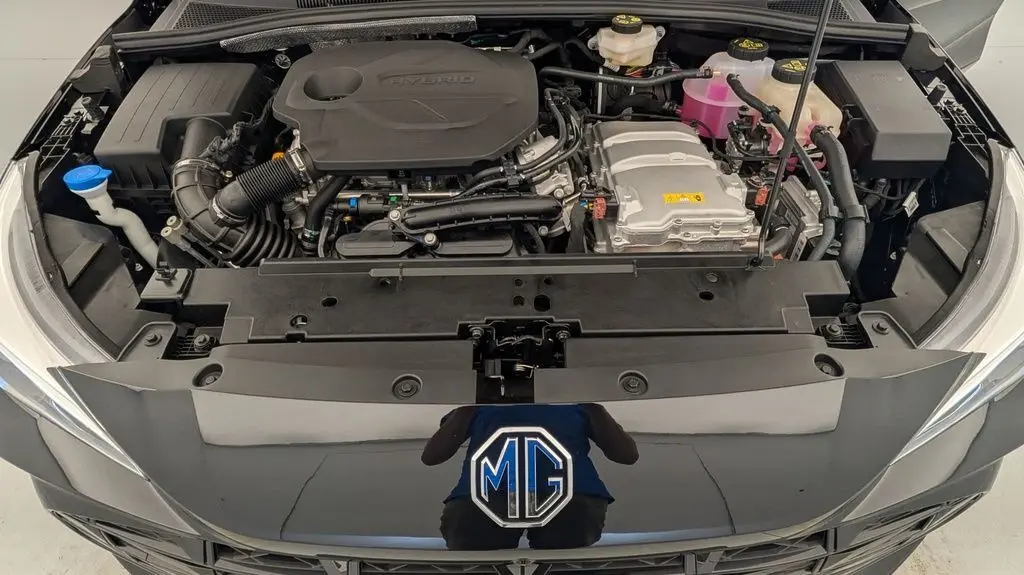 Vue plongeante sur le moteur hybride du MG3 Pebble Black, avec capot ouvert et logo MG visible sur la calandre noire.