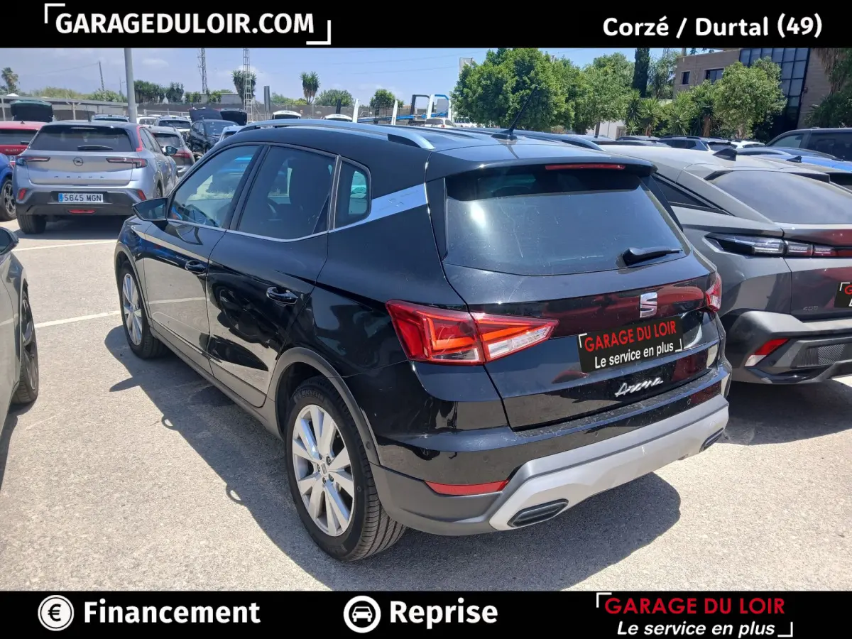 Vue 3/4 arrière droite d'un SEAT Arona noir avec toit et rails argentés, garé en extérieur sur parking.