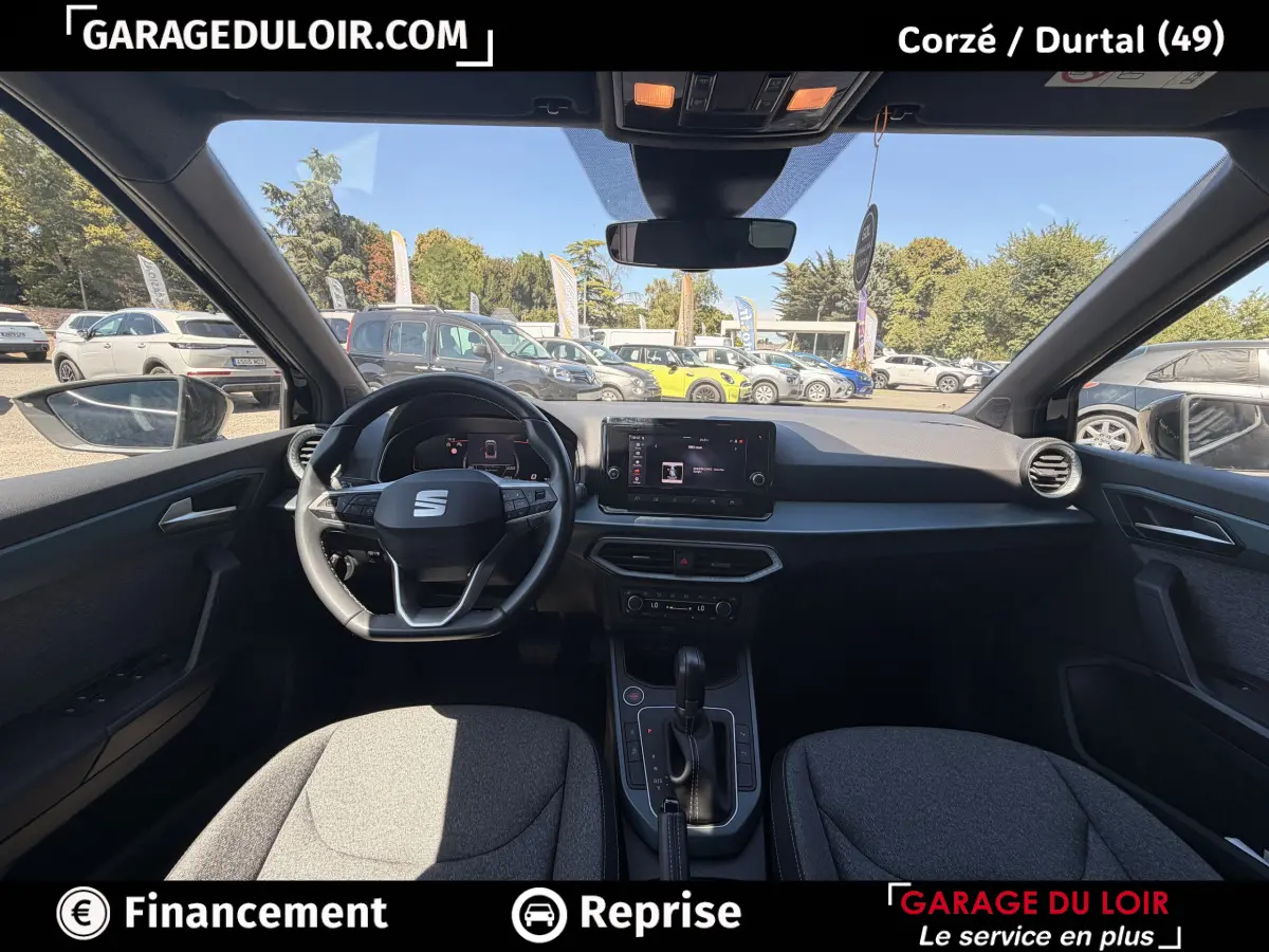 Vue intérieure avant du SEAT Arona noir 2025, tableau de bord moderne avec écran tactile et volant multifonctions.
