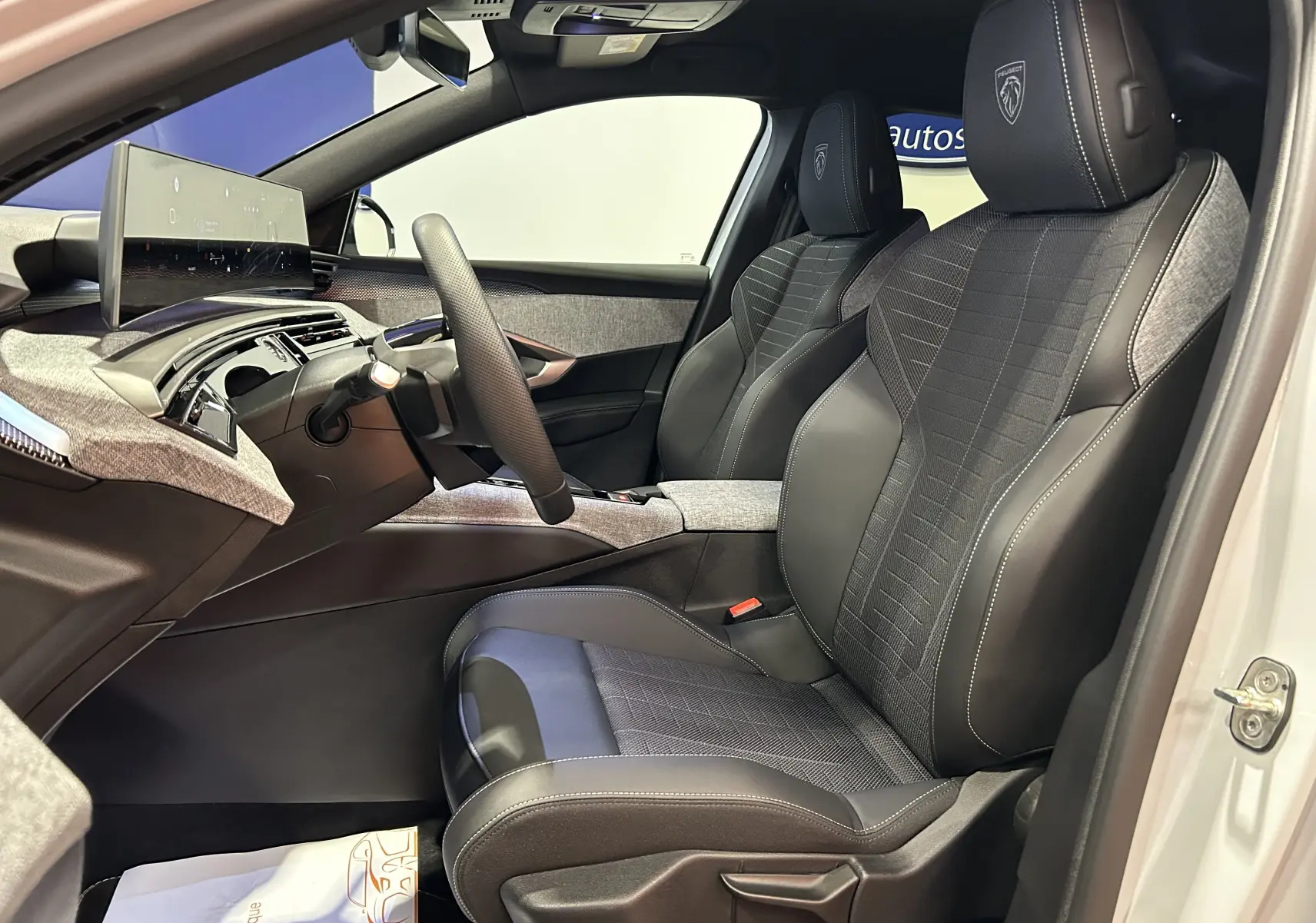 Vue intérieure côté conducteur du Peugeot 3008 Hybrid 2026, sièges bi-matière avec logo Peugeot brodé sur appuie-tête.