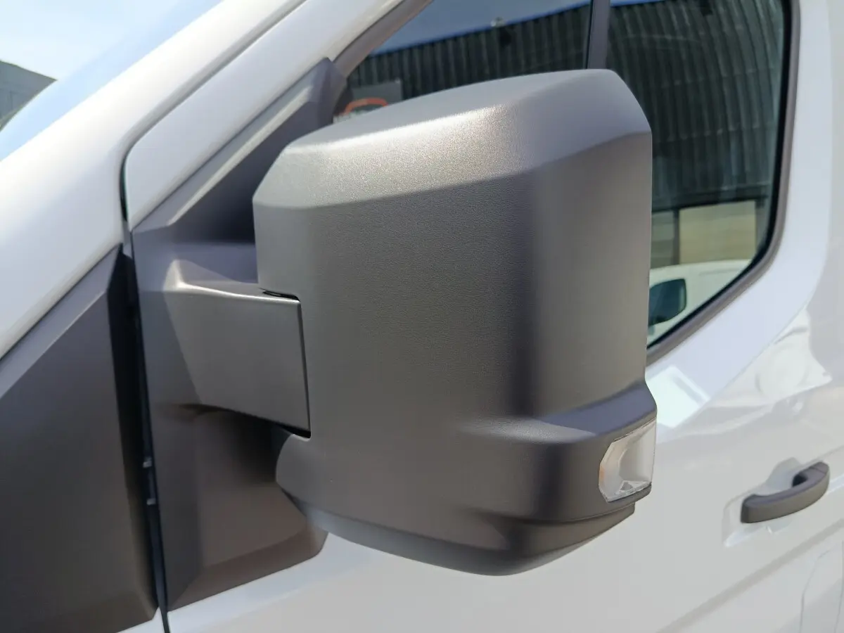 Rétroviseur droit noir en gros plan sur Renault Master blanc, avec porte et fenêtre visibles en arrière-plan.
