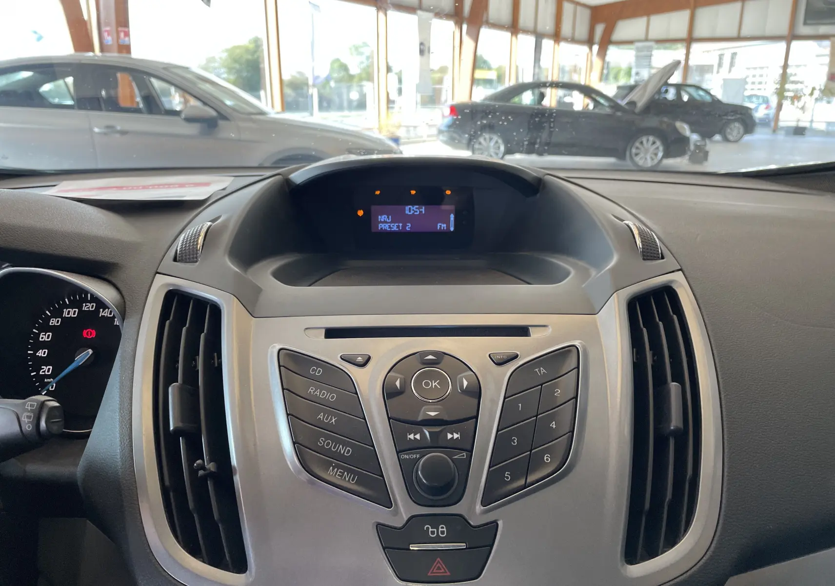 Tableau de bord central du Ford C-MAX gris 2012 avec commandes audio et écran digital affichant la radio FM.