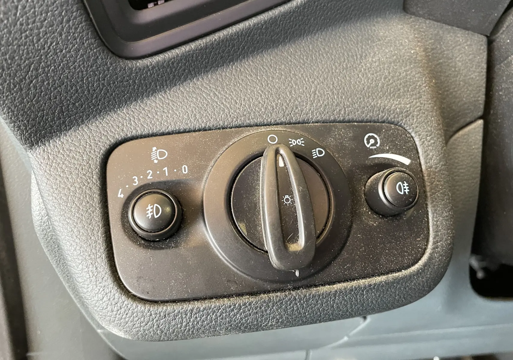 Gros plan sur le bouton de commande des phares noir dans l'habitacle du Ford C-MAX gris 2012.