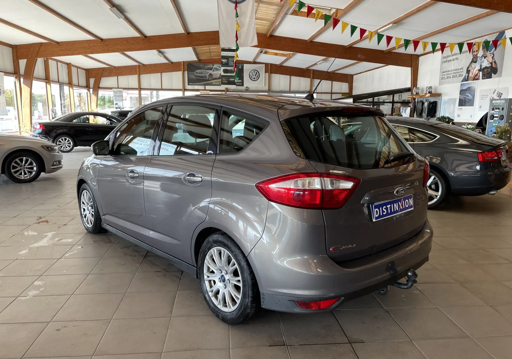 Ford C-MAX gris vue 3/4 arrière droit dans un showroom, avec attelage de remorque visible.