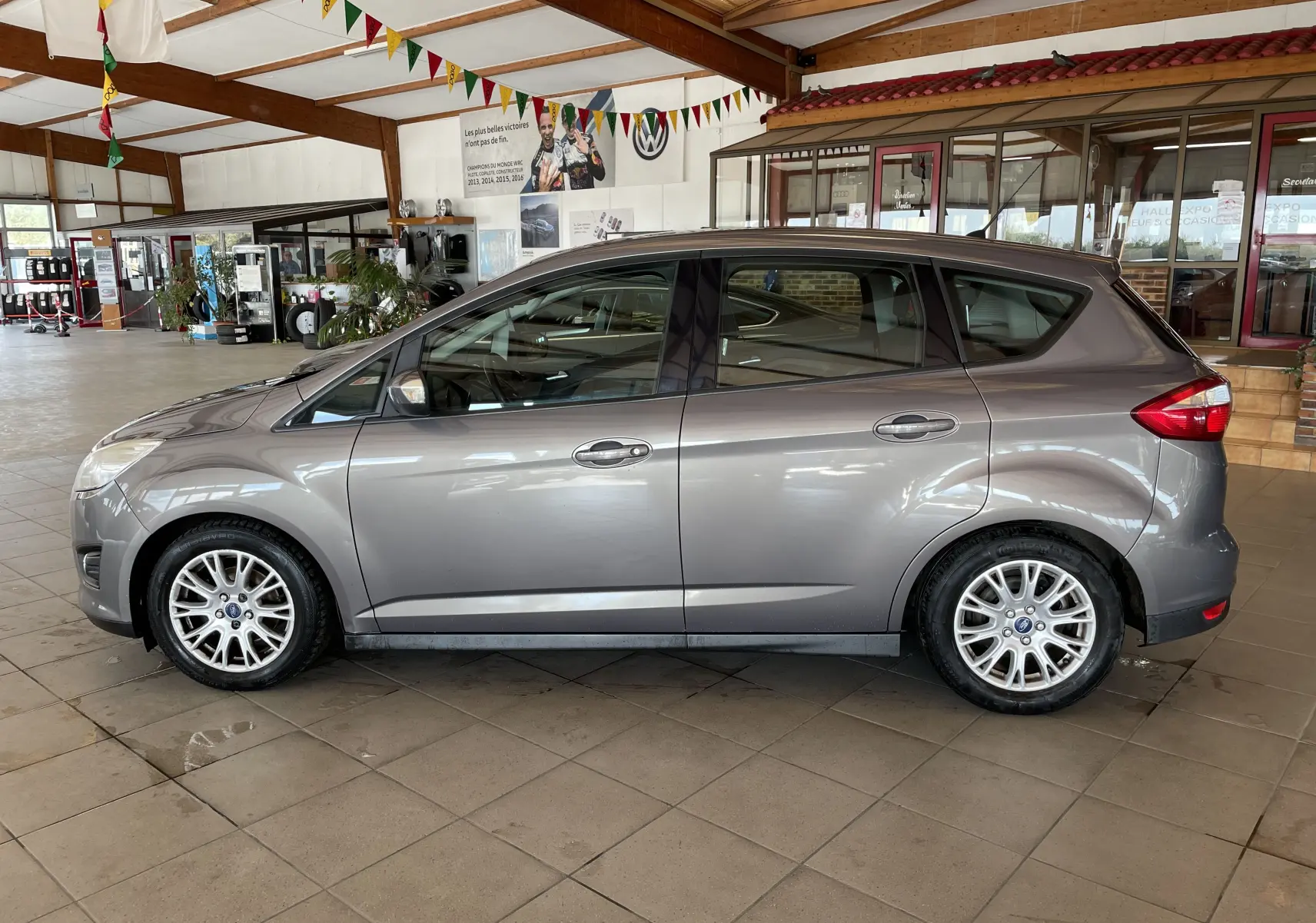 Vue de profil côté gauche d'un Ford C-MAX gris 2012 diesel en intérieur, avec jantes alliage et vitres teintées.