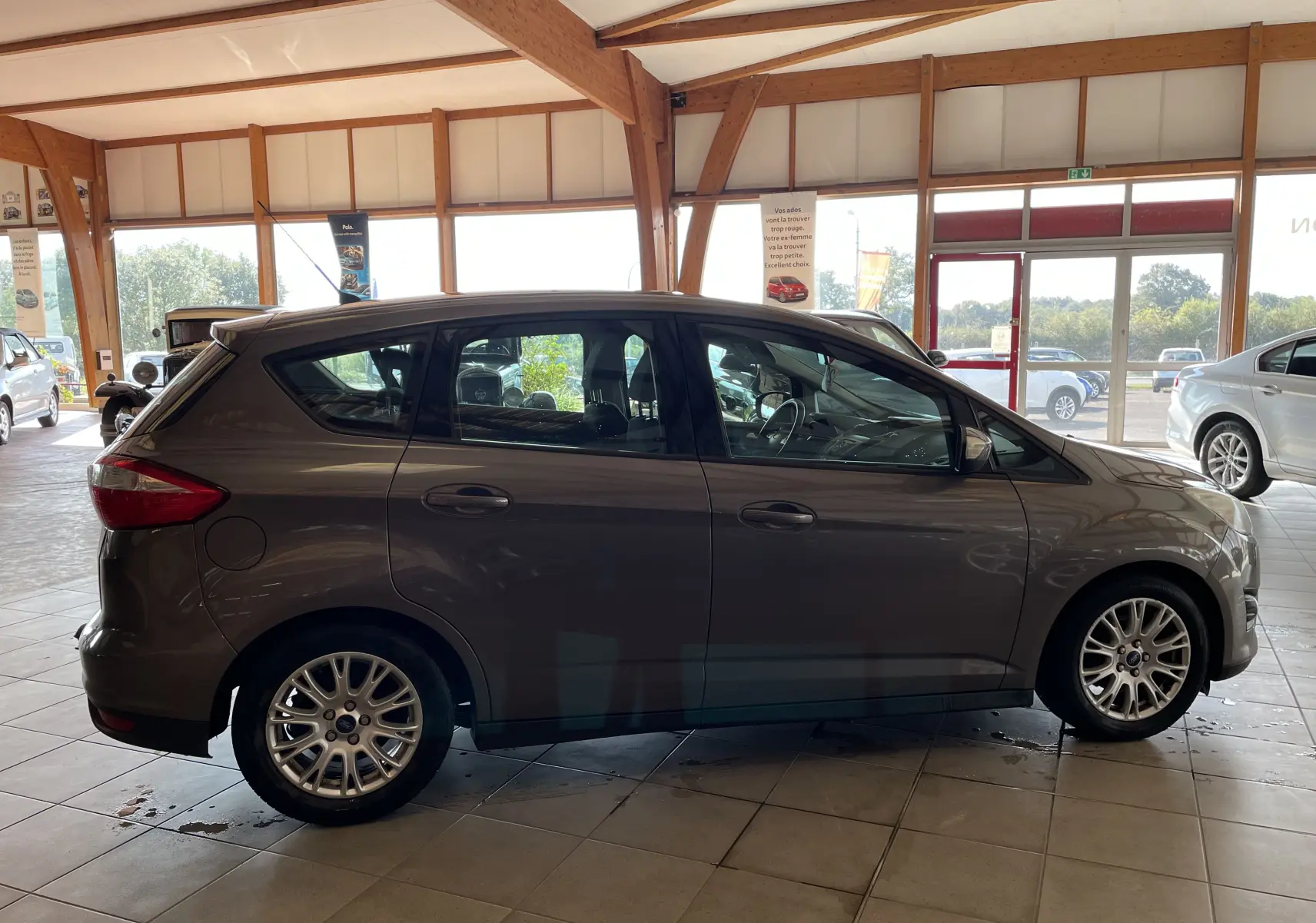Ford C-MAX gris vue de profil côté gauche dans un showroom, soulignant ses jantes alliage et lignes compactes.