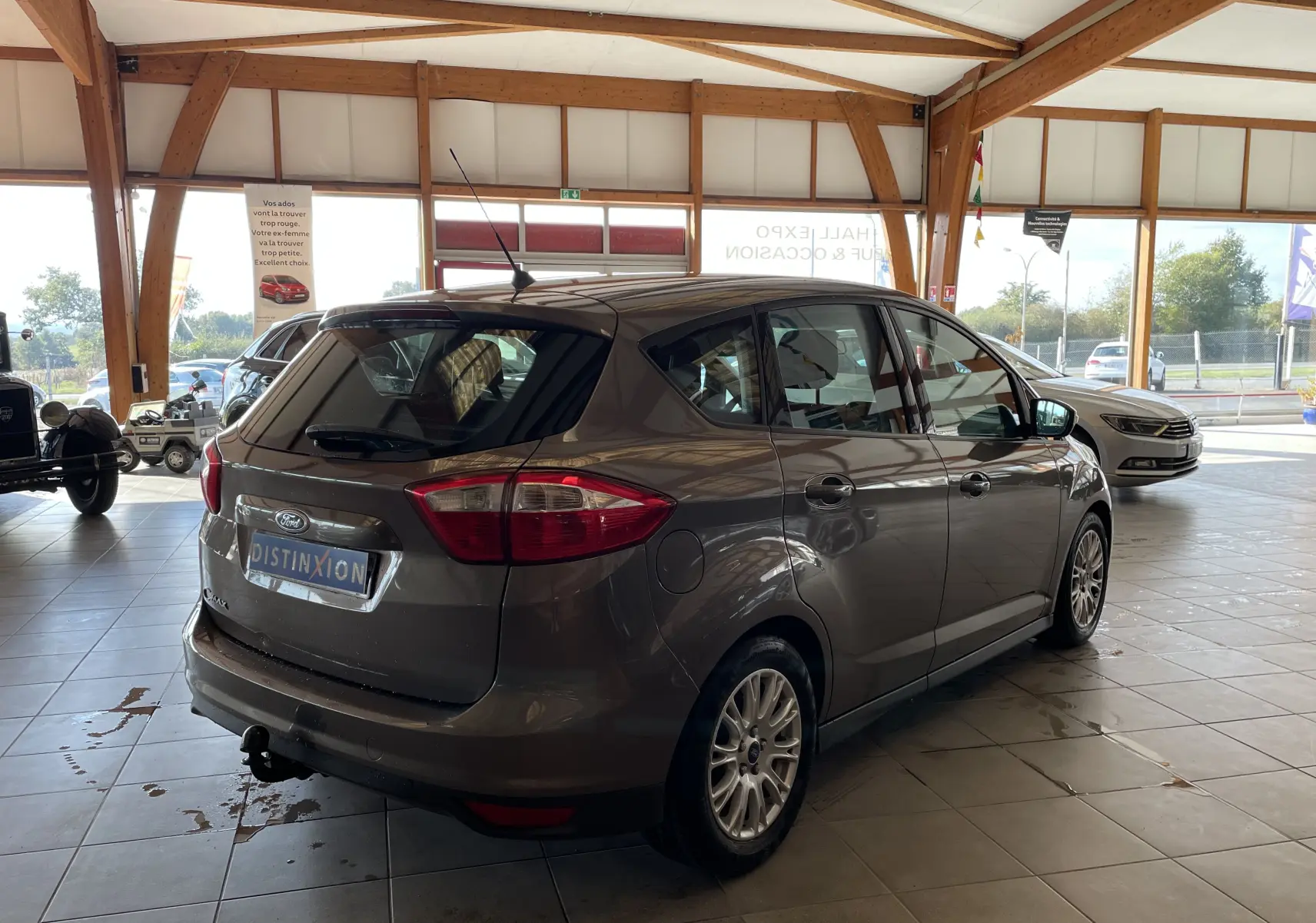 Ford C-MAX gris vue 3/4 arrière droit en intérieur, avec attelage et jantes alliage visibles.