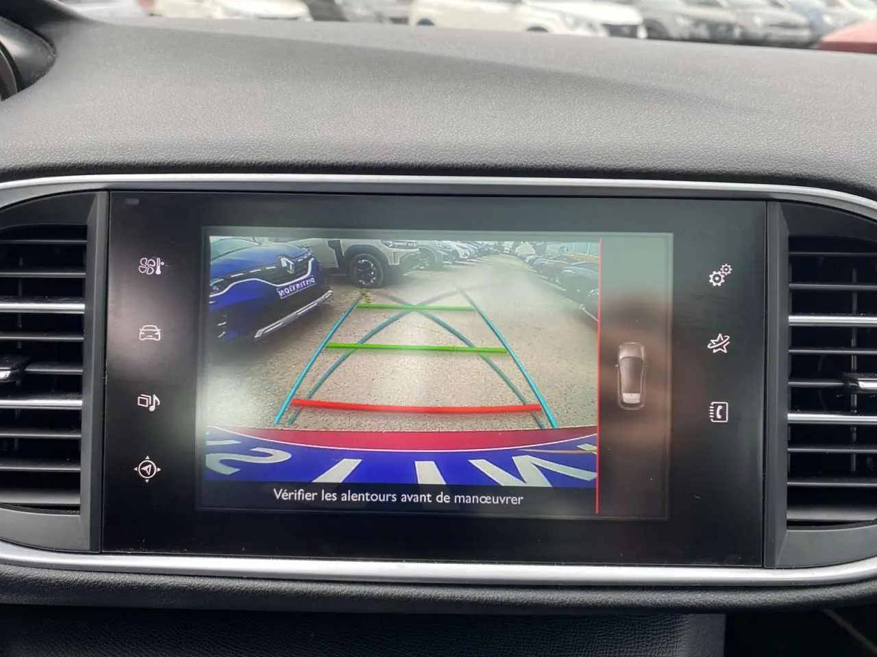 Écran central montrant la caméra de recul active d'une Peugeot 308 rouge avec lignes de guidage colorées.