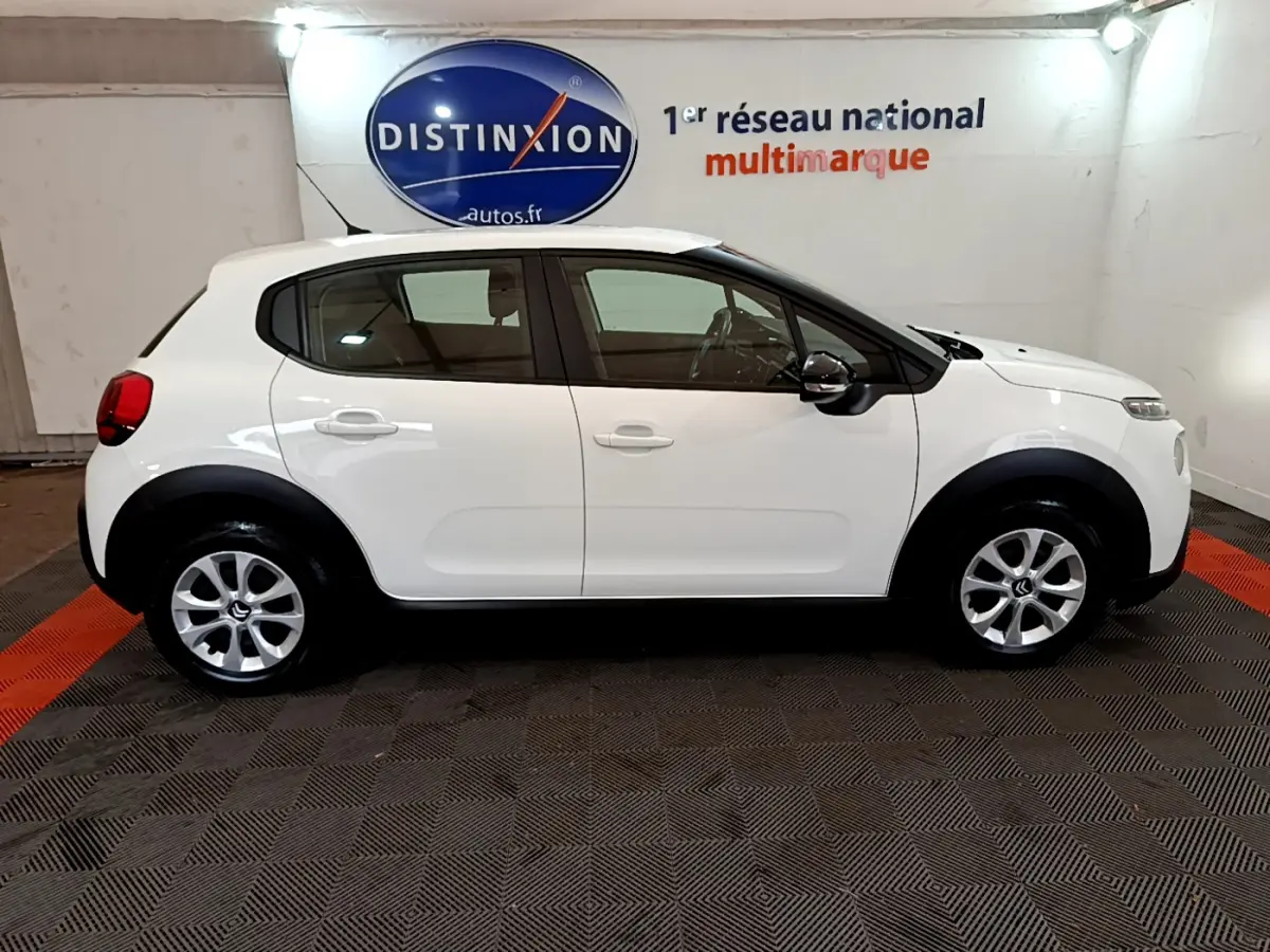 Profil côté gauche d'une Citroën C3 blanche PureTech 68 BVM Feel de 2018, en intérieur sur sol damier noir et rouge.