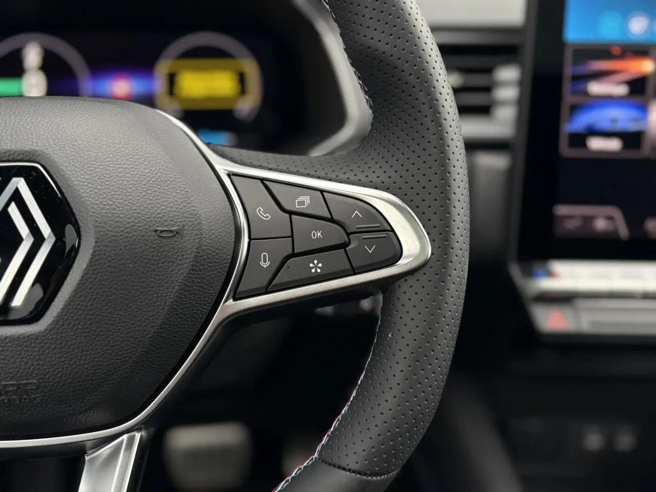 Gros plan sur le volant perforé avec commandes intégrées et logo Alpine sur Renault Captur hybride 2025.