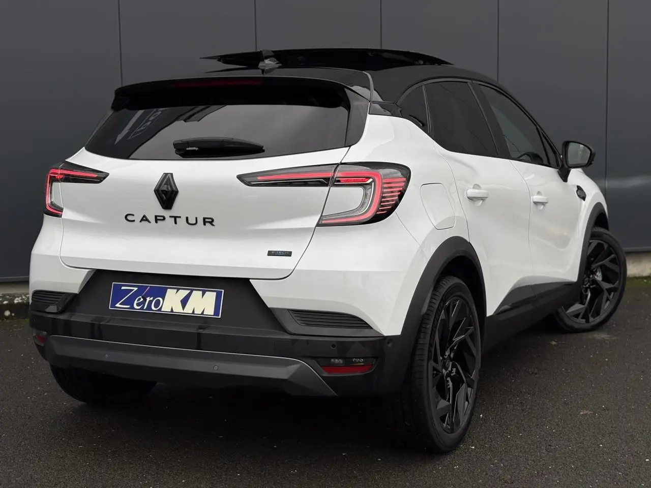 Vue 3/4 arrière droite du Renault Captur blanc nacré avec toit noir étoile et jantes noires distinctives.