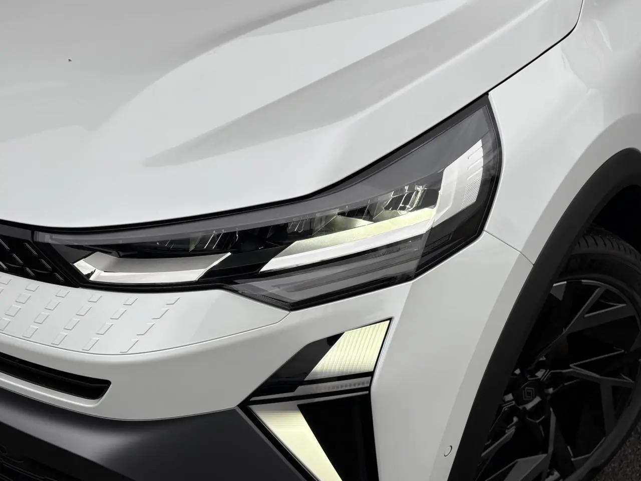 Gros plan sur l'avant droit du Renault Captur blanc nacré, mettant en valeur le phare LED et la jante noire design.