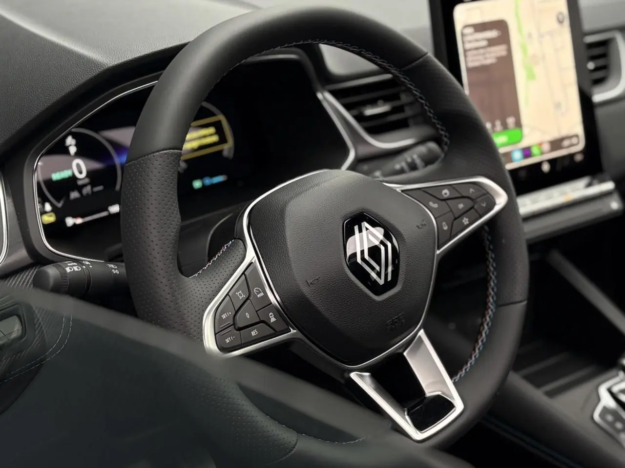 Gros plan sur le volant noir avec surpiqûres tricolores du Renault Captur 2025, tableau de bord numérique et écran tactile visibles.