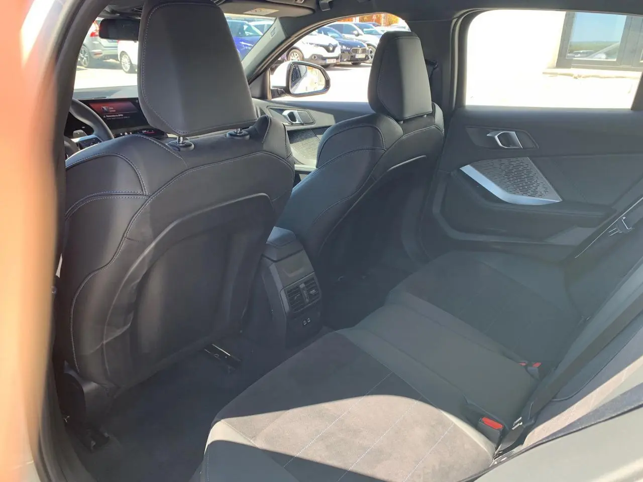 Vue intérieure arrière côté droit de la BMW Série 1 118D M Sport blanche avec sellerie Alcantara noire et surpiqûres bleues.