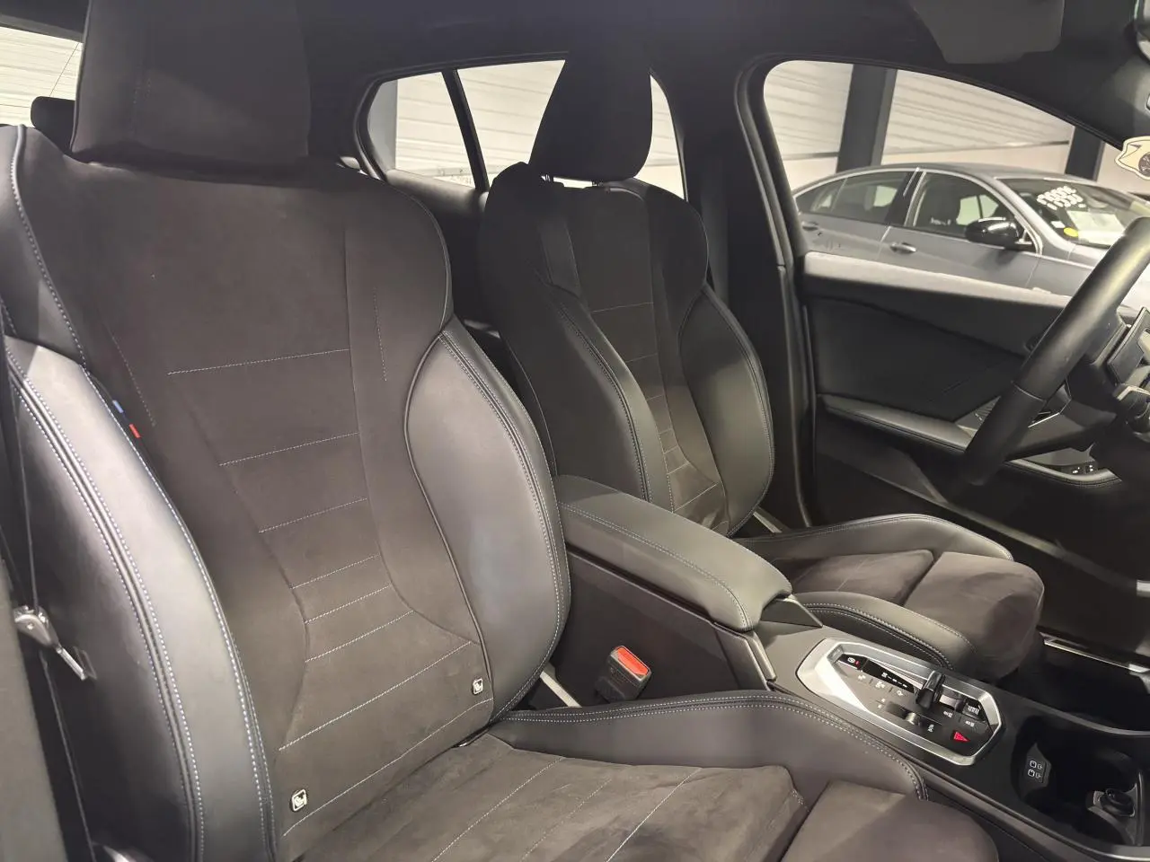 Vue intérieure sur les sièges avant sport en Alcantara noir avec surpiqûres bleues et console centrale de la BMW Série 1.
