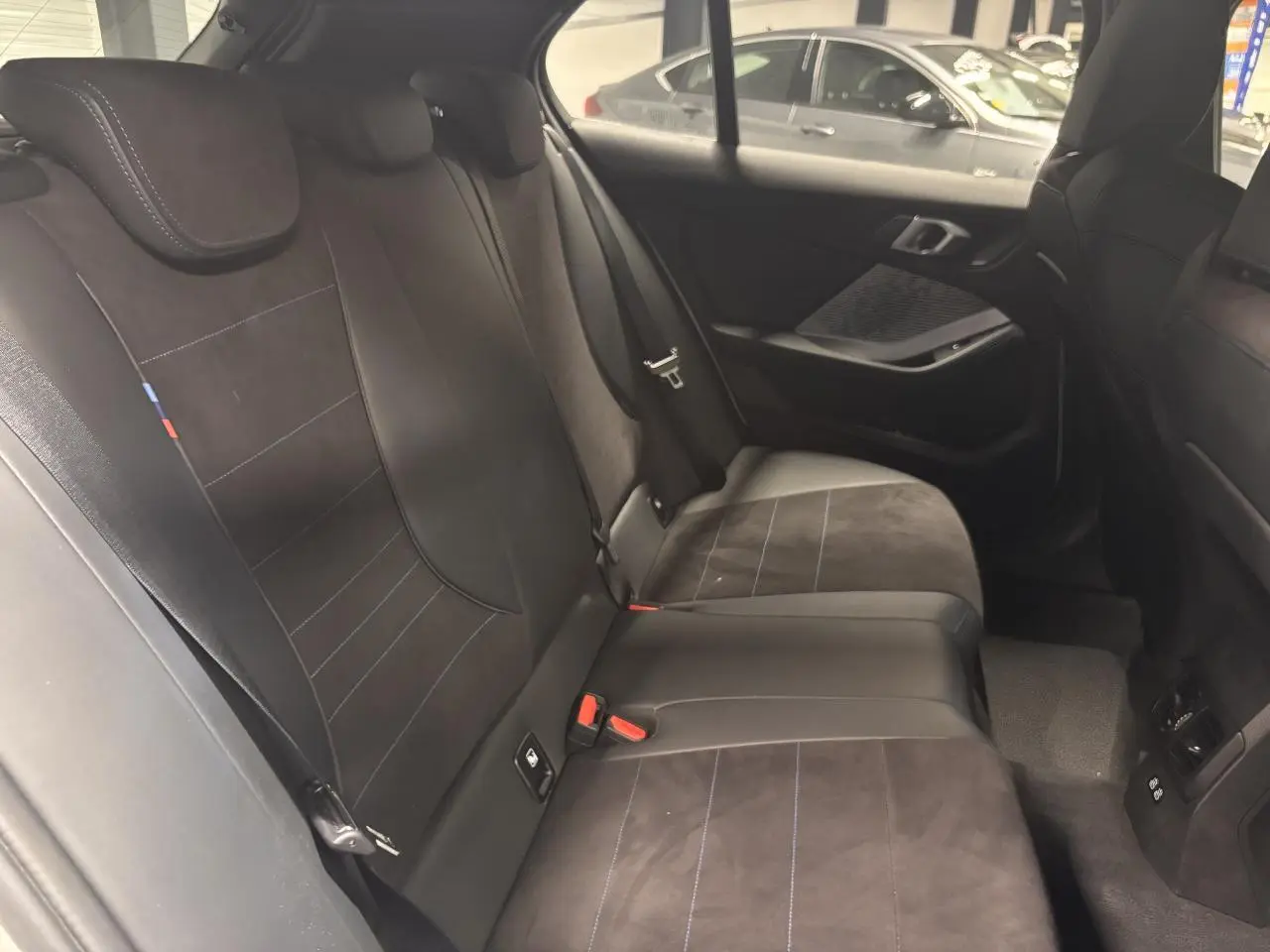 Vue intérieure côté droit des sièges arrière en Alcantara noir avec surpiqûres bleues de la BMW Série 1 118D M Sport 2025.