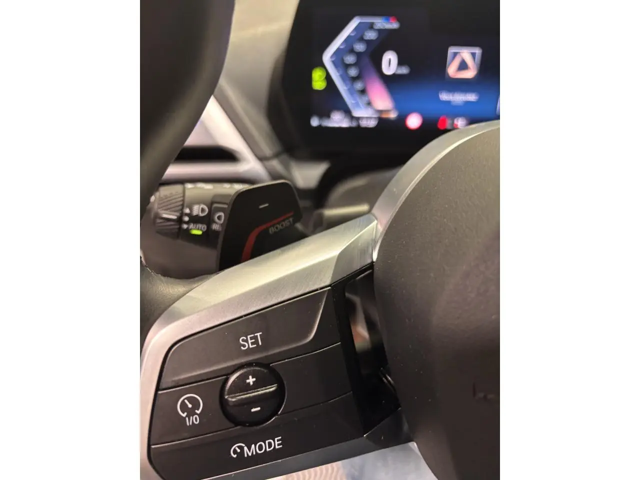 Gros plan sur les commandes du volant à gauche de la BMW Série 1 118D blanche, avec affichage numérique en arrière-plan.