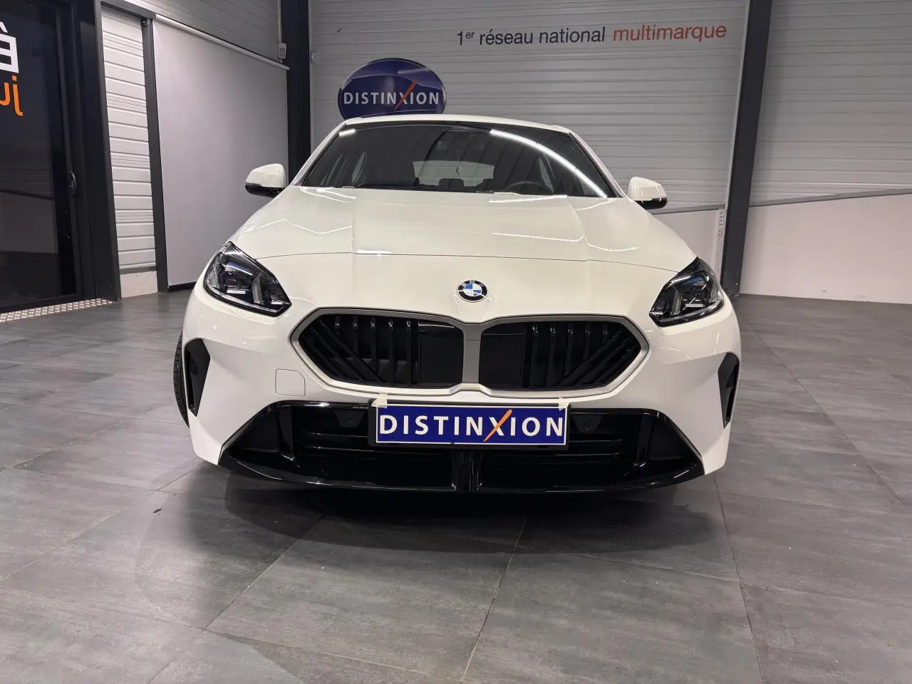 Vue avant d'une BMW Série 1 118D blanche avec calandre noire et projecteurs LED dans un showroom.