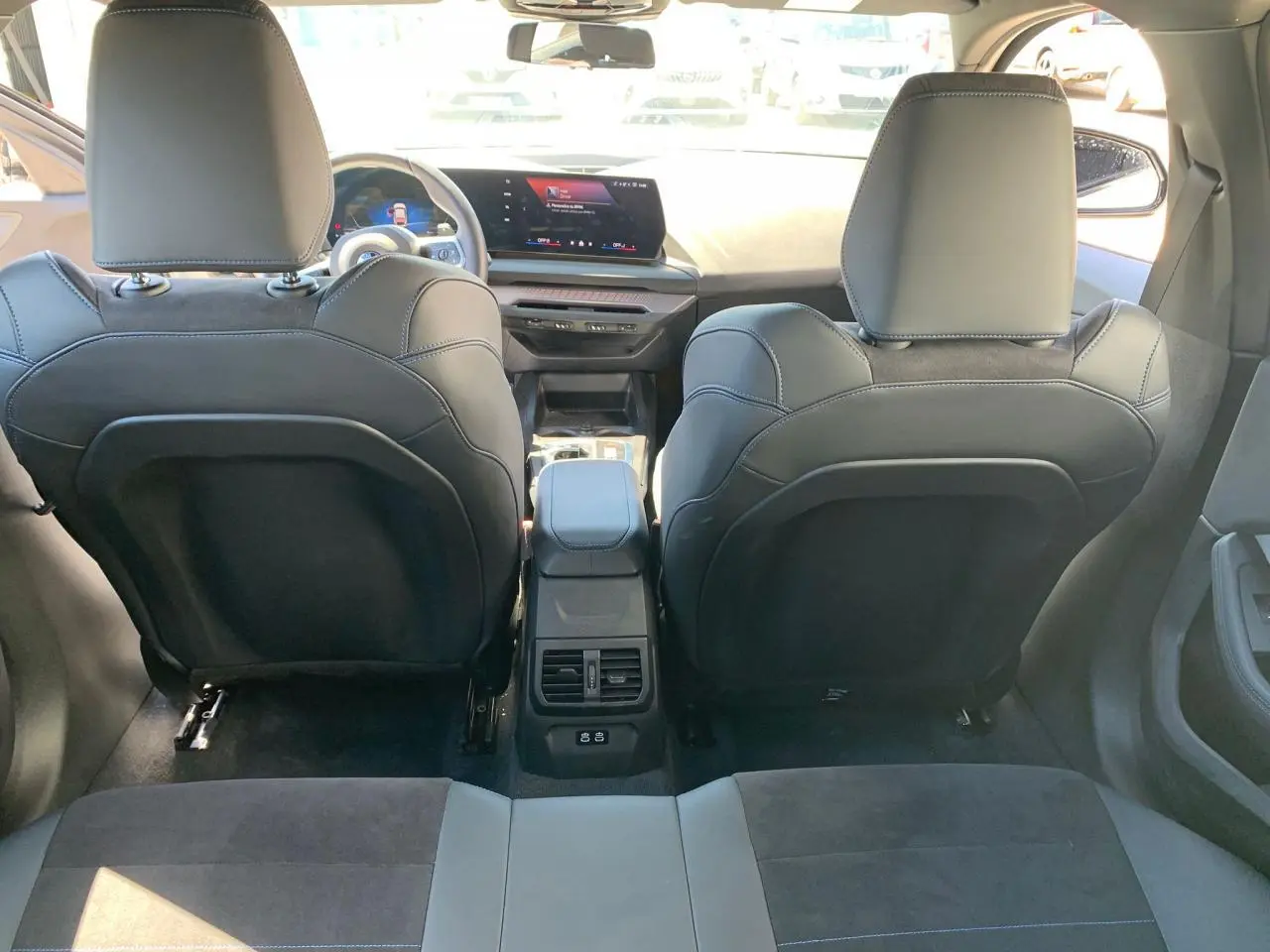 Vue arrière de l'intérieur noir Alcantara d'une BMW Série 1 118D 2025 avec console centrale et écran tactile.