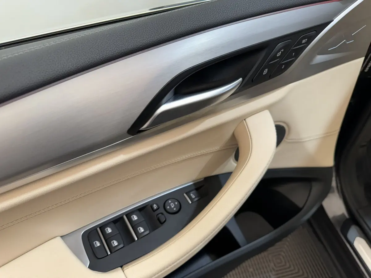 Détail de la porte avant gauche beige et noire du BMW X3 xDrive30d 2018 avec commandes électriques et insert aluminium.