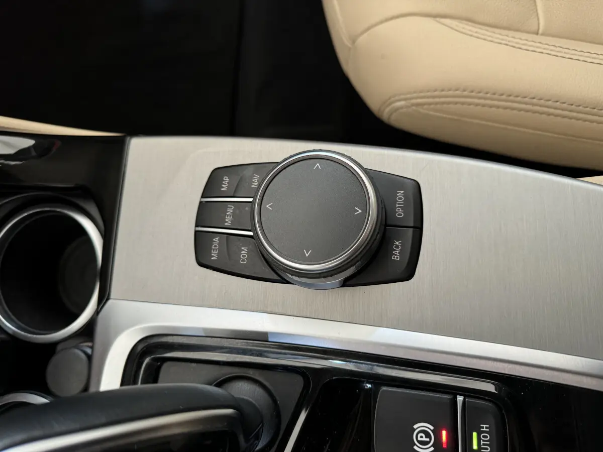 Gros plan sur la molette de commande iDrive et les boutons autour, console centrale en aluminium brossé, siège beige BMW X3 2018.