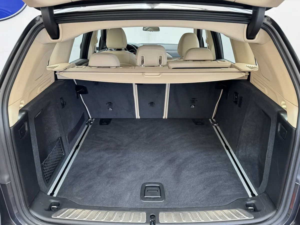 Vue arrière du coffre spacieux et propre avec habillage beige et tapis noir dans un BMW X3 gris foncé 2018.