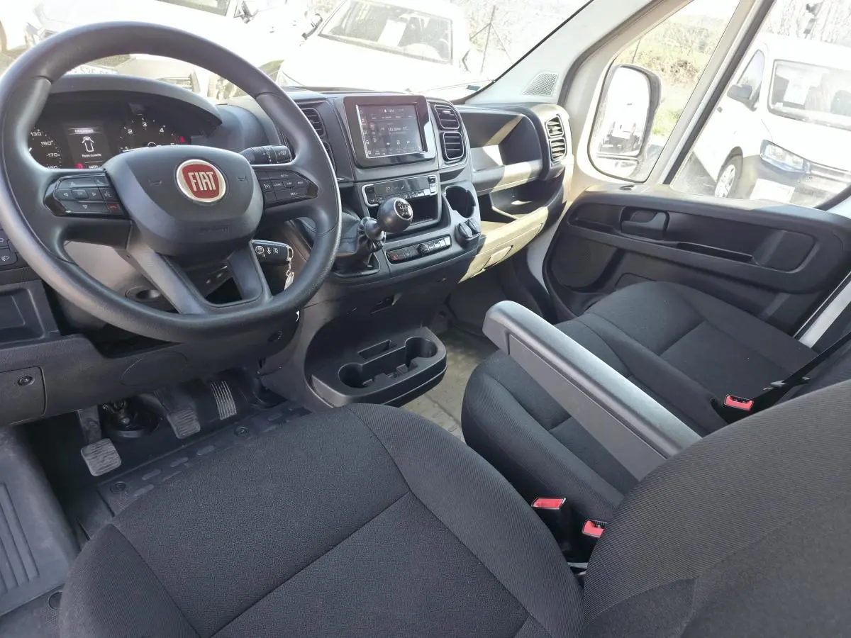 Vue intérieure côté conducteur du Fiat Ducato Fourgon blanc 2023, avec volant multifonction et écran tactile central.