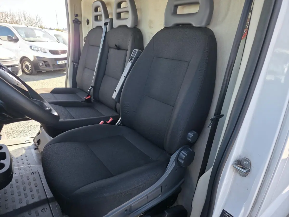 Vue intérieure côté conducteur du Fiat Ducato Fourgon blanc 2023, montrant les sièges noirs et la cloison tôlée arrière.