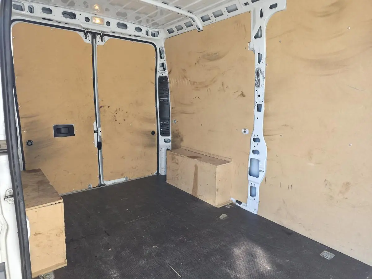 Intérieur du fourgon FIAT Ducato Maxi blanc vu de l'arrière, montrant la cloison tôlée et le revêtement bois des parois.