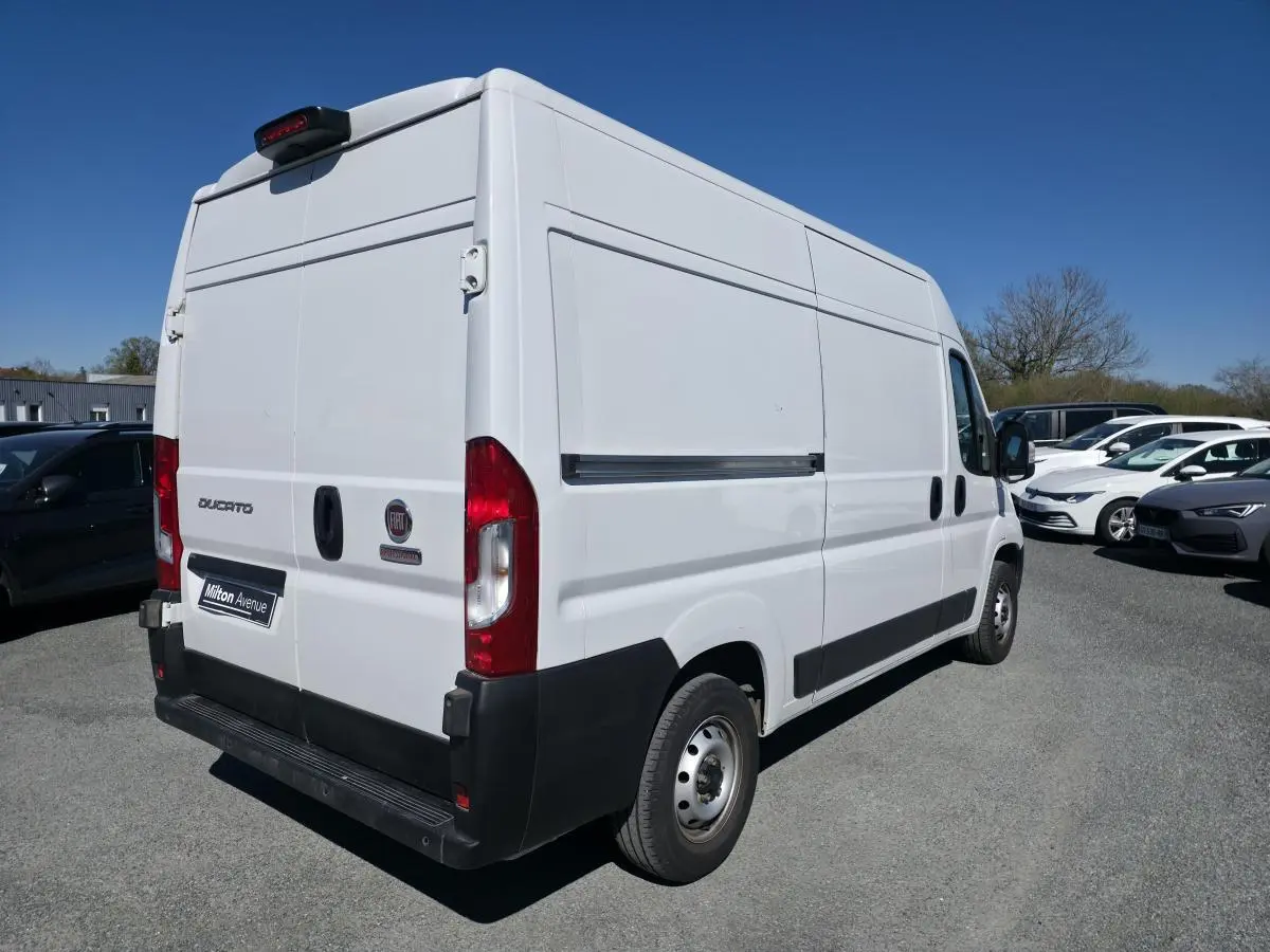 Vue 3/4 arrière droite d'un FIAT Ducato Fourgon blanc tôlé Maxi avec porte latérale coulissante, sur parking extérieur.
