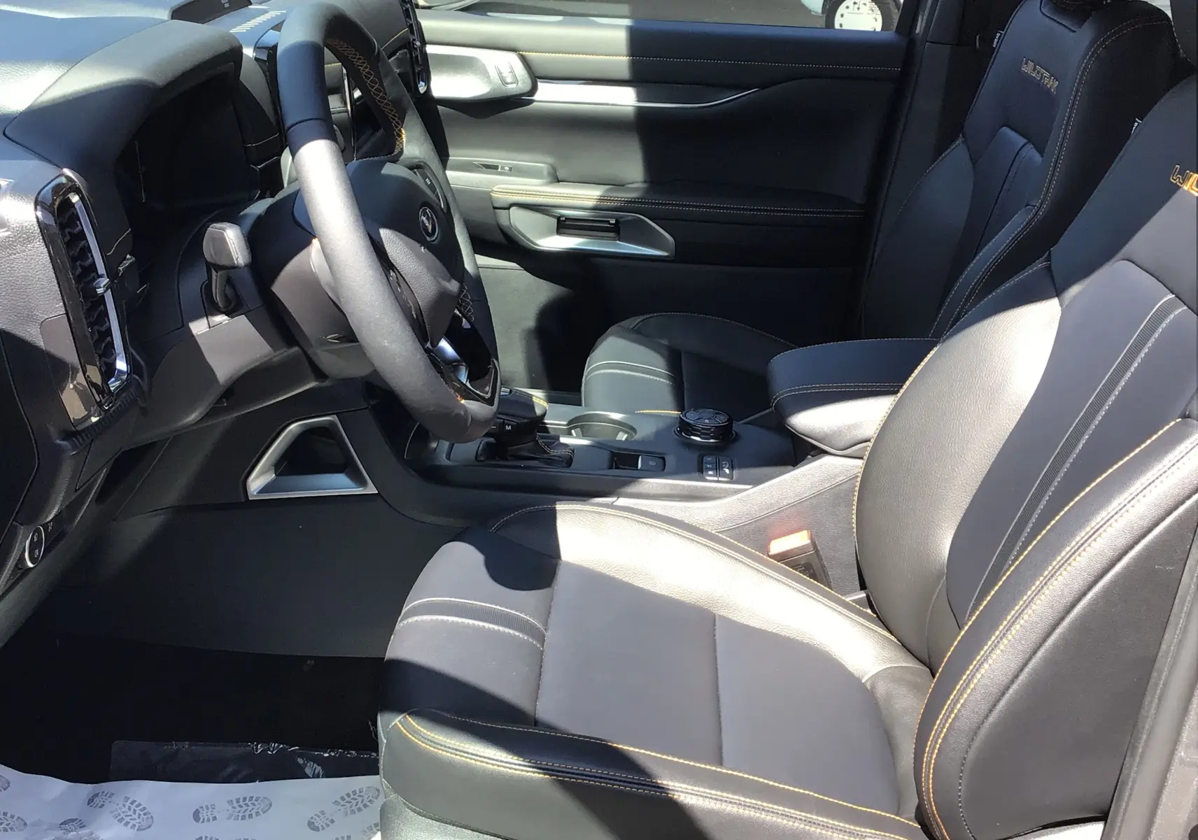 Intérieur du Ford Ranger Wildtrak 2025 montrant les sièges cuir noirs avec surpiqûres orange et tableau de bord côté conducteur.