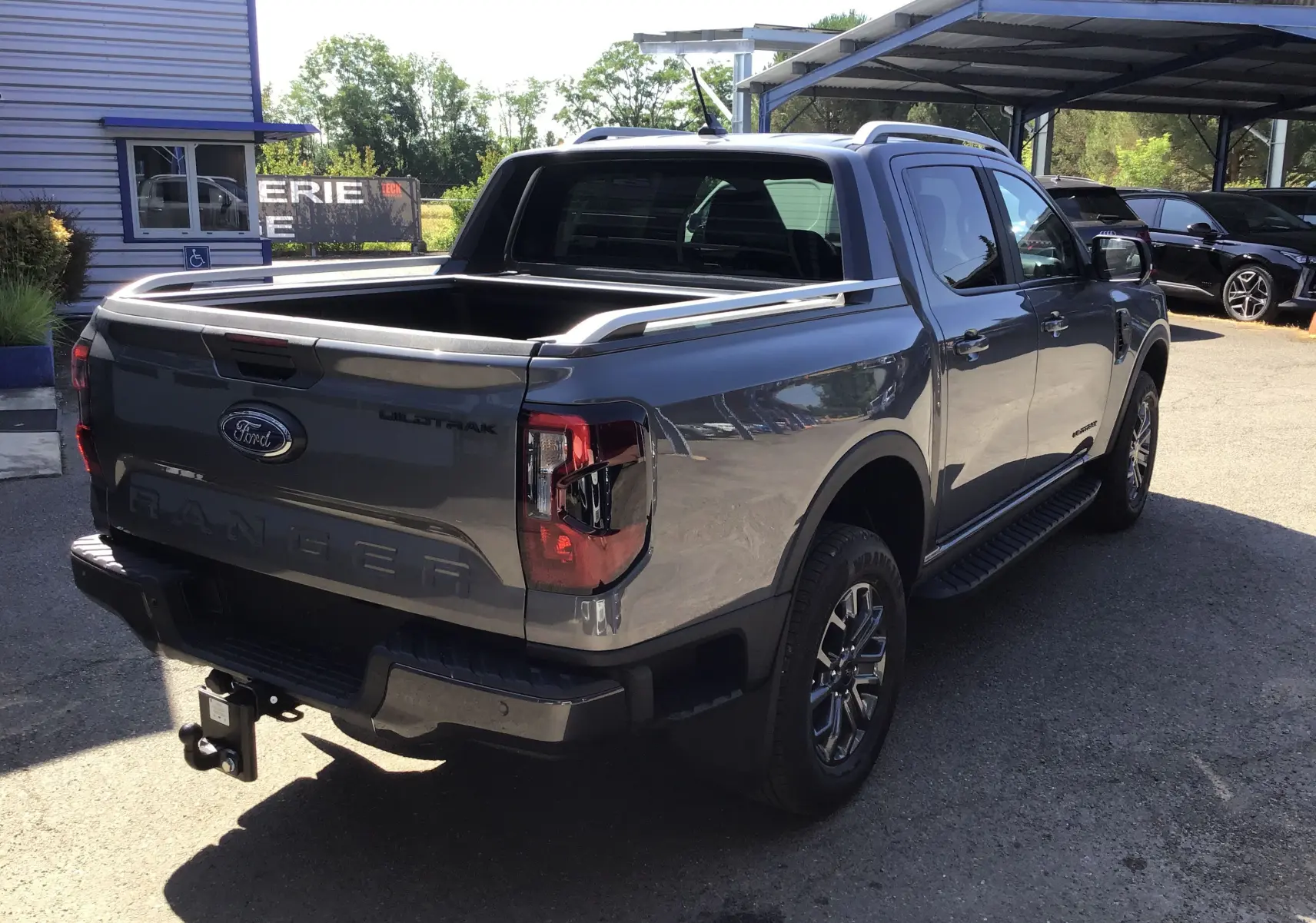 Vue 3/4 arrière droite du Ford Ranger Double Cabine gris carbone avec benne ouverte et attelage visible.