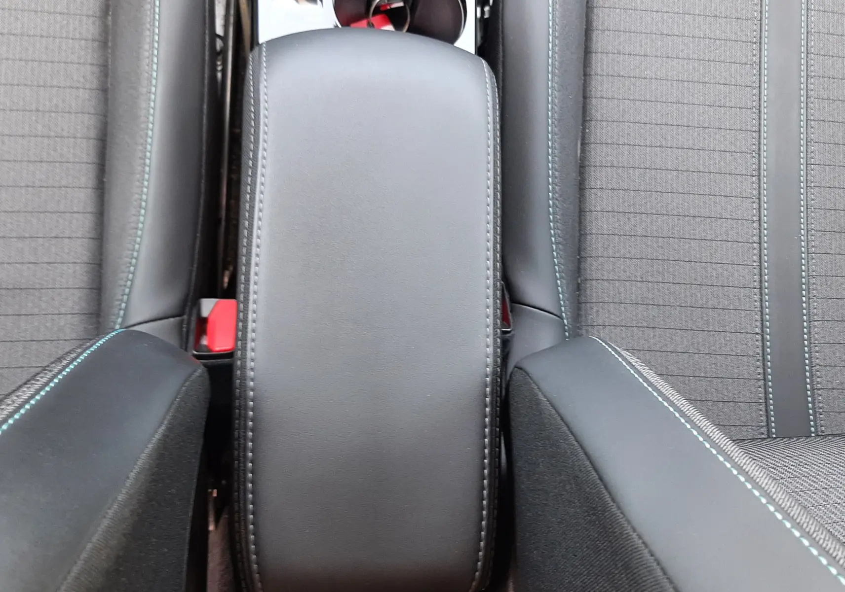 Vue plongeante sur l'accoudoir central noir et les sièges tissu gris avec surpiqûres bleues d'un Peugeot 2008 2022