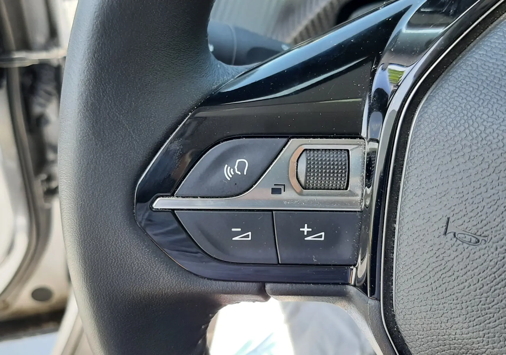 Gros plan sur les commandes du volant à gauche du Peugeot 2008 gris Artense, avec boutons de volume et commande vocale.