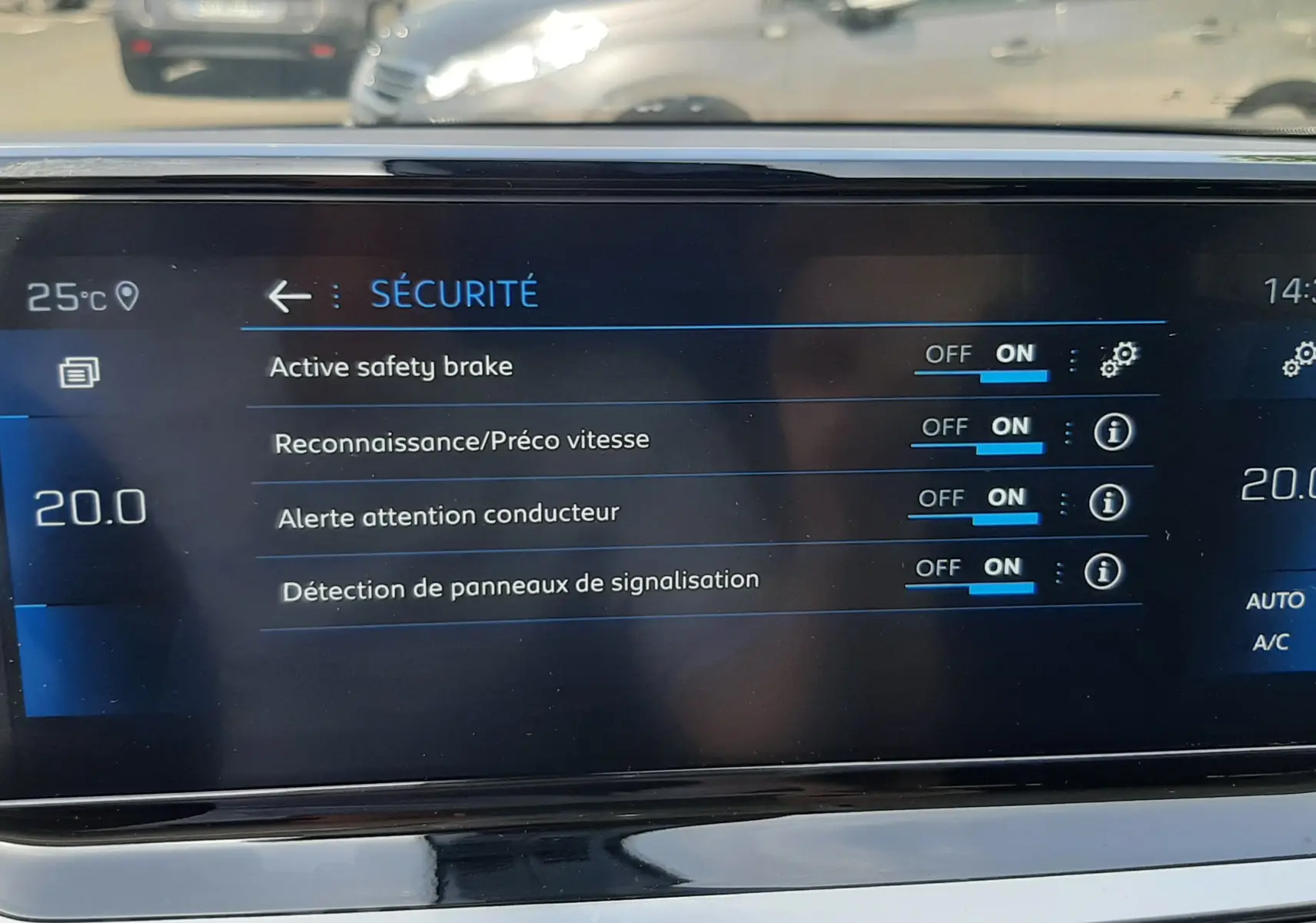 Écran central du Peugeot 2008 2022 montrant les réglages de sécurité avec vue floue sur parking extérieur en arrière-plan.