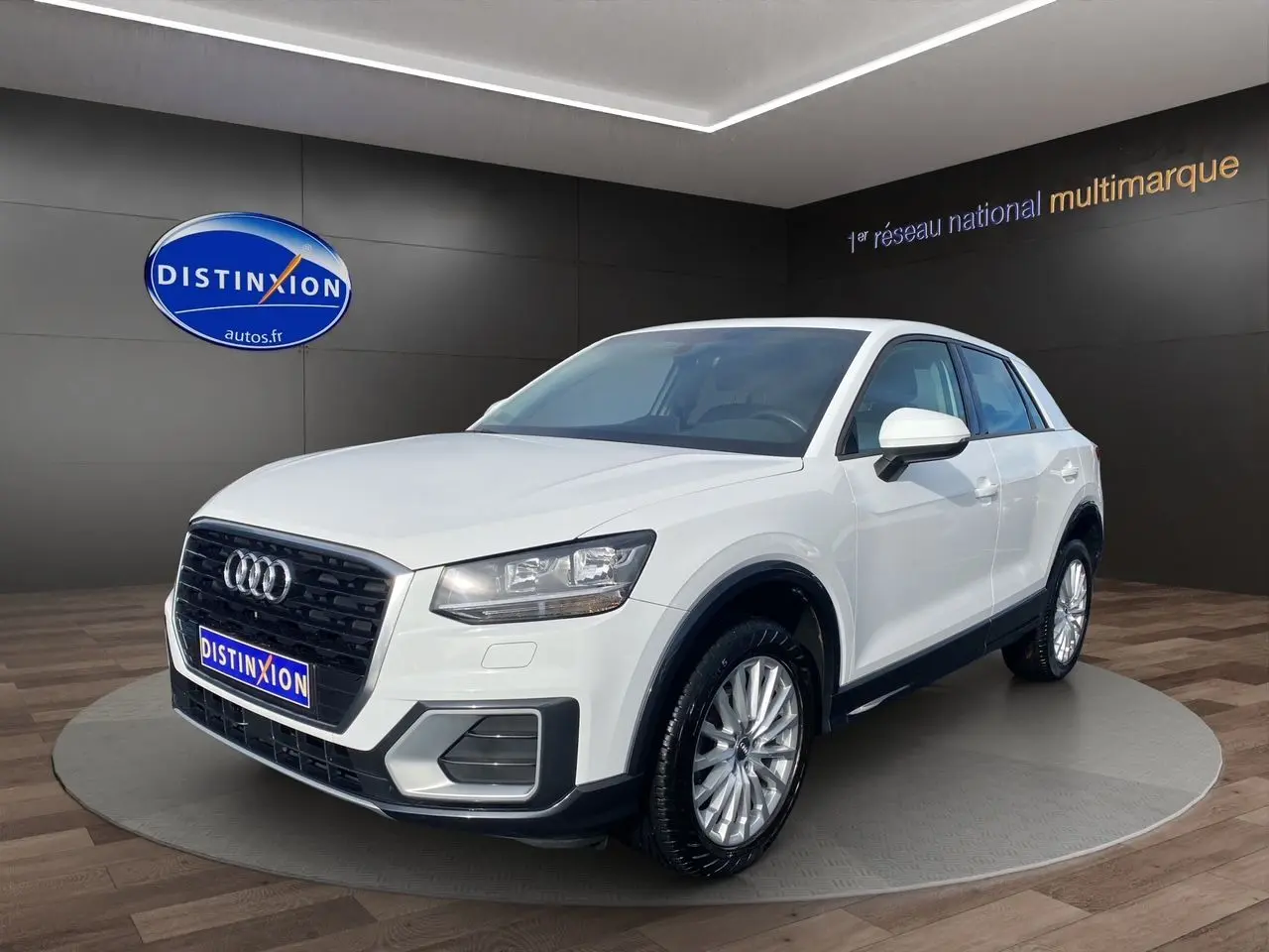 Audi Q2 blanc vue 3/4 avant droit en intérieur avec calandre noire et jantes argentées multibranches.