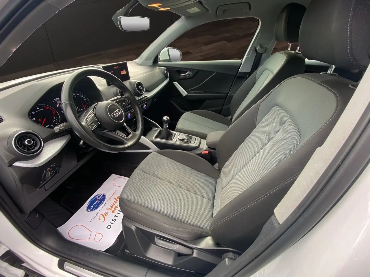 Vue intérieure côté conducteur de l'Audi Q2 30 TDI 2019 avec sièges tissu gris et volant multifonction noir.