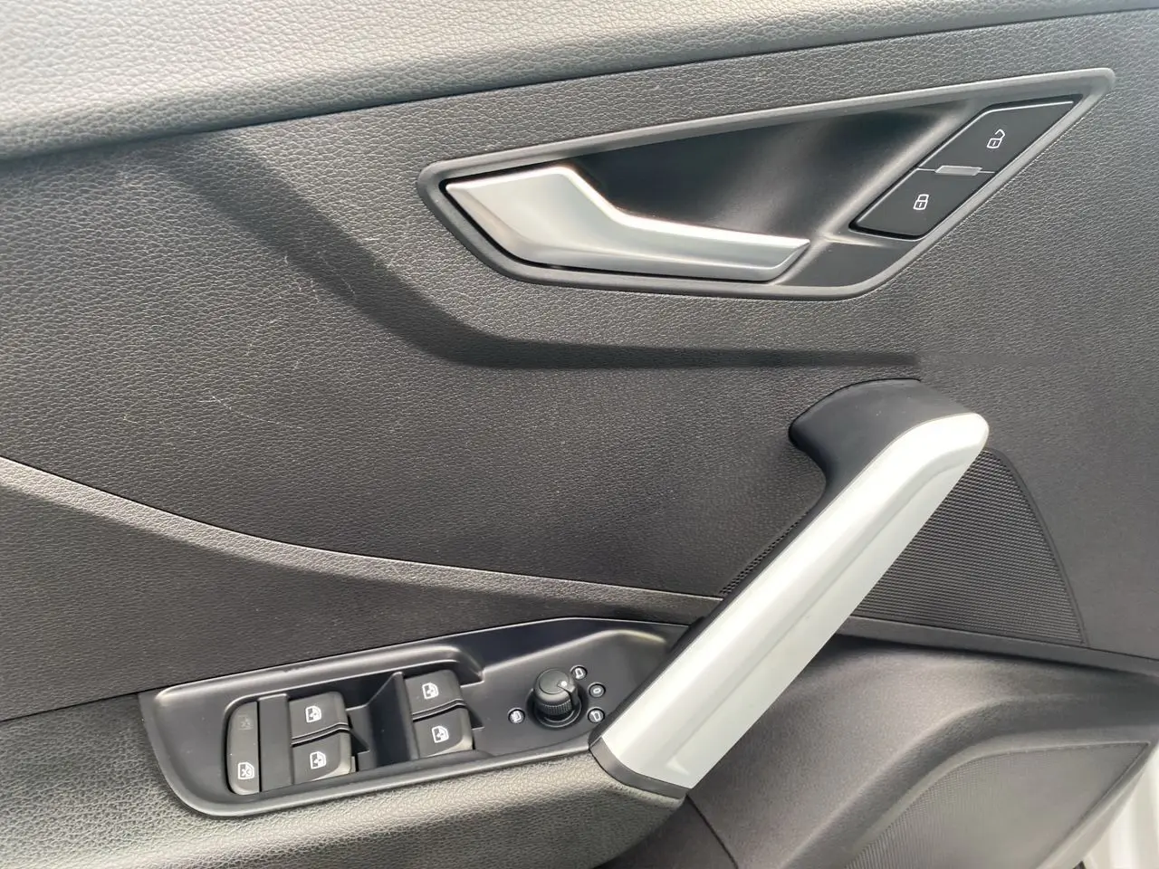 Poignée de porte intérieure côté gauche de l'Audi Q2 blanc, avec commandes de vitres et verrouillage intégrées.