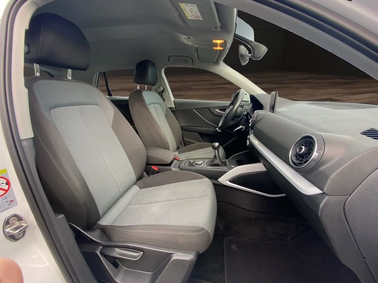 Vue intérieure côté conducteur de l'Audi Q2 30 TDI 2019 avec sièges tissu gris et tableau de bord noir.