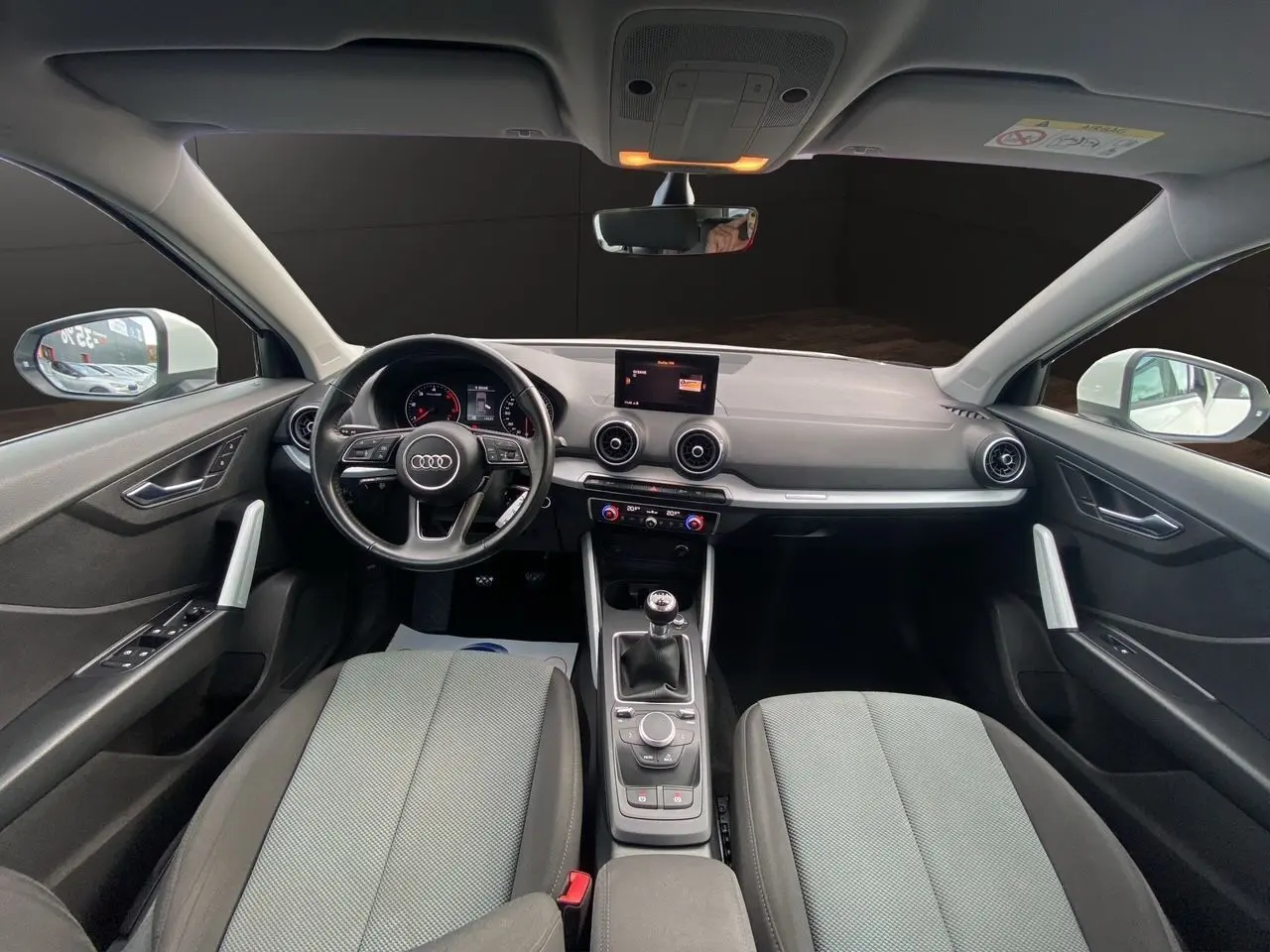 Vue intérieure avant de l'Audi Q2 30 TDI blanc, avec tableau de bord moderne et sièges tissu gris foncé.